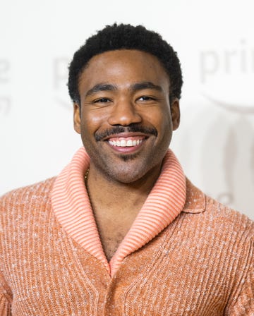 donald glover wears an orange sweater and smiling for a photo