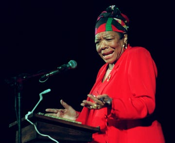 maya angelou wearing a red dress and gesturing with her hands as she reads poetry at a podium