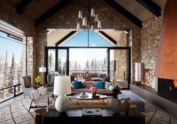 great room with high ceilings and large glass windows and a fireplace on the right and a furniture and seating gathering in the center and a view of the snowy mountains