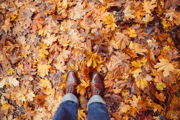 a person's feet in brown leather boots on a pile of leaves