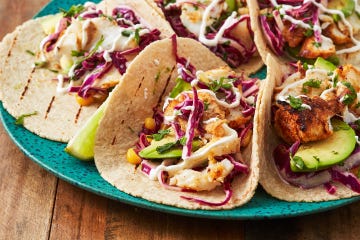 fish tacos with corn, avocado, red cabbage slaw, and sour cream drizzle on a teal plate