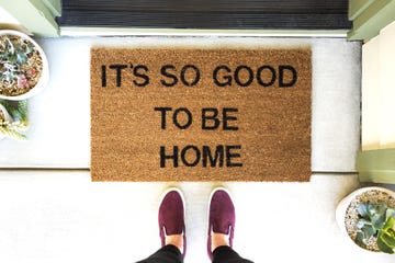 person standing in front of a welcome mat that says it's so good to be home