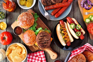 summer bbq food table scene with hot dog and hamburger buffet top view over a dark wood background