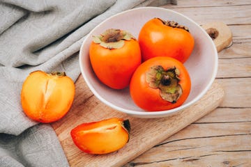 fresh ripe persimmons in white bowl on cutting board and napkin on wooden table healthy vegan food concept top view