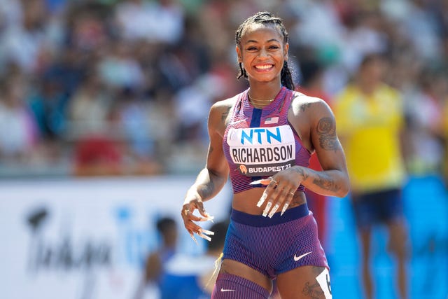 a woman in a purple and blue uniform who smiles and has her hands out in front of her torso