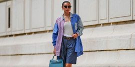 person wearing a multicolored oversized shirt and shorts carrying a teal handbag