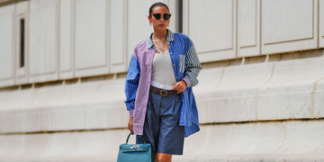 person wearing a multicolored oversized shirt and shorts carrying a teal handbag