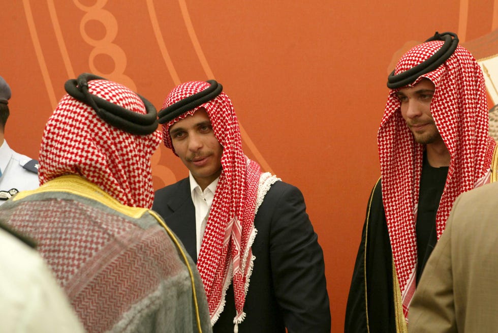 prince hamzah bin hussein of jordan talks with an unidentifiable person whose back is facing the camera, prince hamzah wears a dark suit jacket, white collared shirt and a red and white headscarf