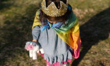 three year old girl with crown and rainbow cape on carrying unicorn toy