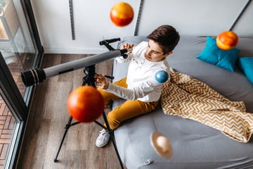 boy sitting on bed looking into telescope with planet mobile above his head