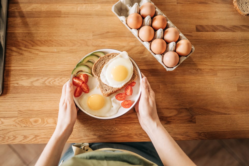 girl hands above frying pan with three cooked eggs, herbs, cheese, tomatoes woman is making breakfast top view copy space