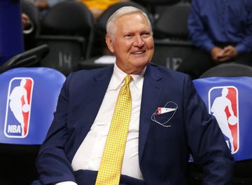 jerry west sitting courtside at a basketball game with the nba logo on chairs