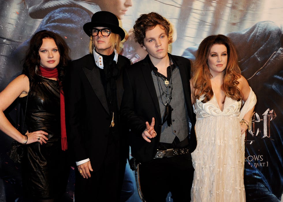 ben keough making a peace sign while standing for photos in front of a backdrop next to his mother, lisa marie presley
