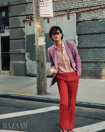 shalom crosses street wearing lavender blazer and pink button up and red trousers