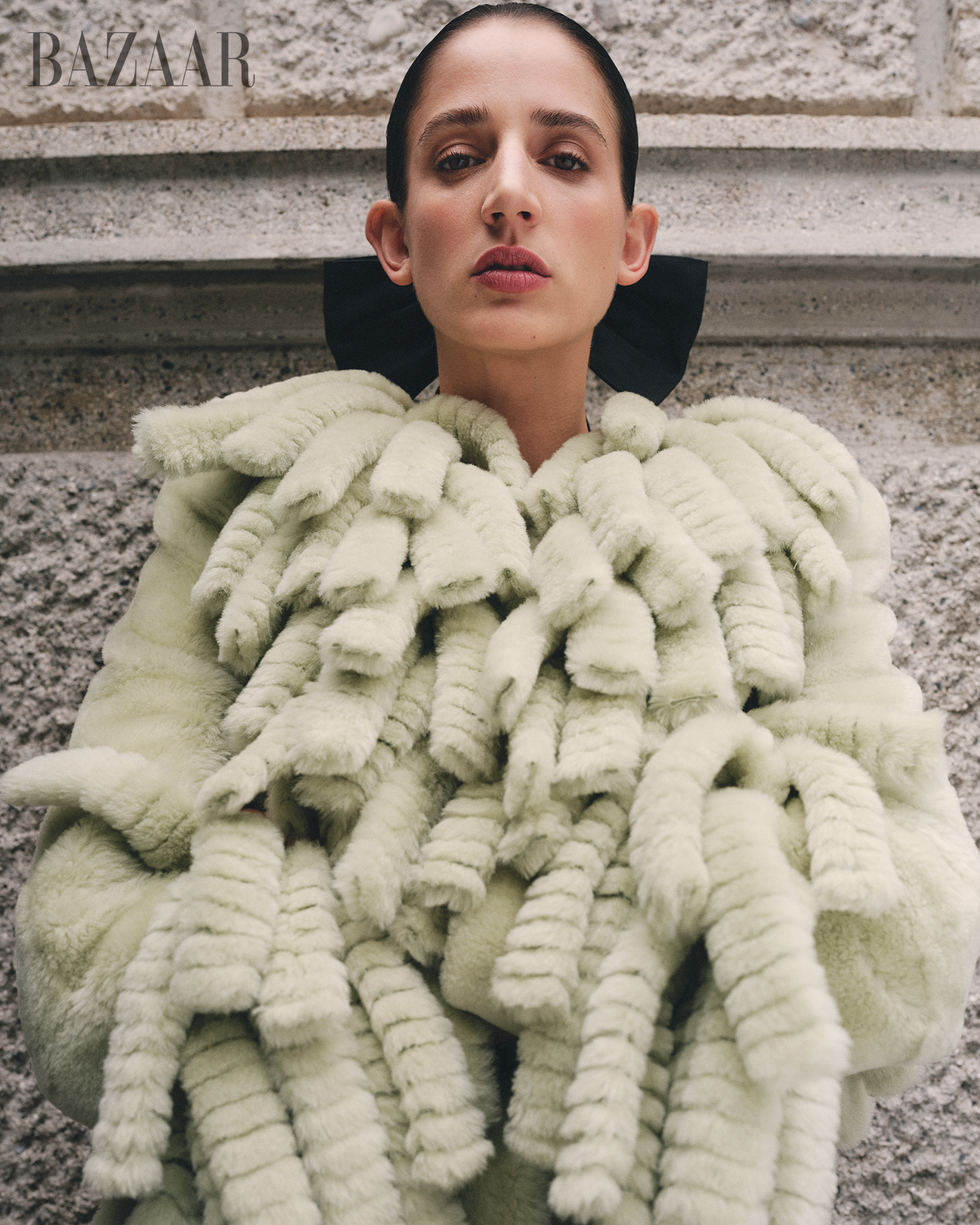 model wearing a textured light green coat with distinct features against a stone backdrop