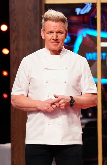 gordon ramsay stands in his chef jacket and looks at the camera, he hands are clasped in front of him