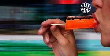 person eating an orange popsicle with a train model on top against a blurred background