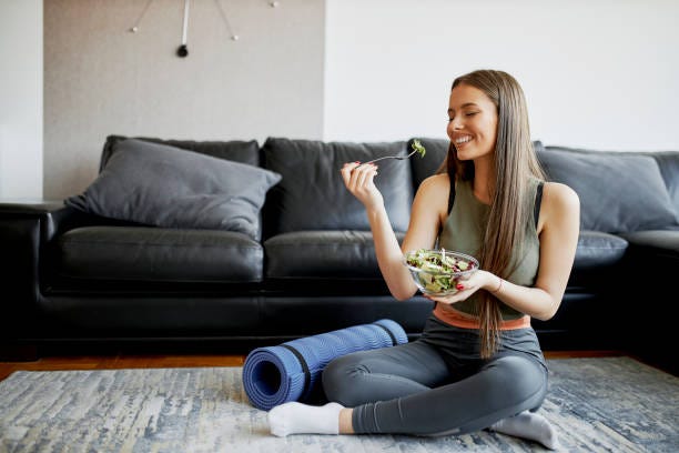 beautiful woman eating fresh salad after intensive home workout