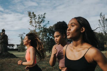 strong, fit woman joggers, running through a sunny park at sunrise they look determined as they put in the effort their hair blows behind them as they look in front of them space for copy