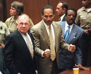 f lee bailey stands and looks left, oj simpson holds his fists in front of him and looks left, johnnie cochran stands and looks left, all three men wear suits with ties