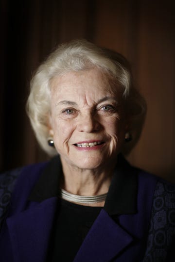 sandra day o'connor smiles at the camera, she wears a purple outfit, a silver necklace, and large earrings