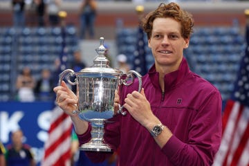 jannik sinner smiles and holds up the us open winner's trophy