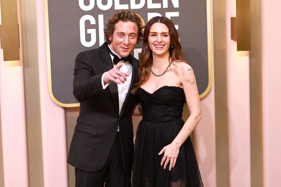 jeremy allen white, wearing a black tuxedo, and addison timlin, wearing a black dress, pose for a photo in front of a golden globes sign