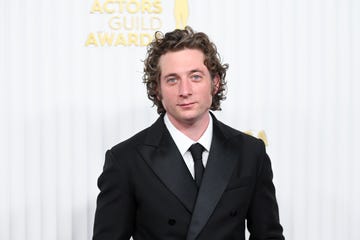 jeremy allen white looks at the camera with a slight smile, he wears a black suit and tie with a white collared shirt