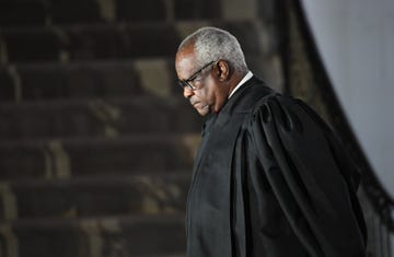 supreme court justice clarence thomas, seen in profile, is standing while wearing his black justice robes and black glasses, he is looking down with a neutral expression on his face