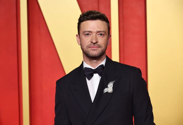 justin timberlake looks at the camera, he weras a black suit jacket and bowtie with a white collared shirt and brooch on his lapel