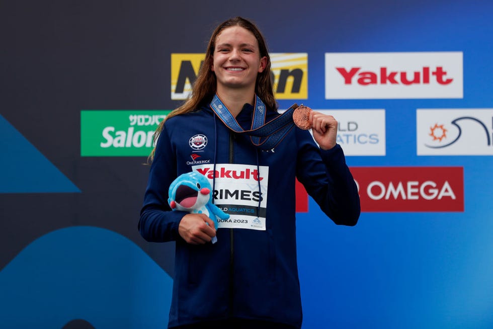 katie grimes holding a medal and stuffed toy and smiling on an award podium