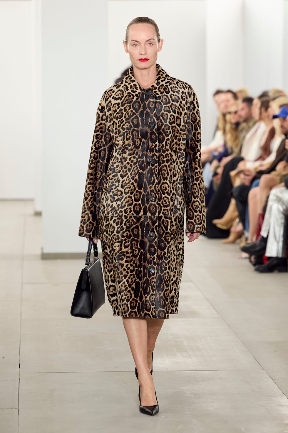 Model walking the runway in a leopard print coat and holding a black handbag