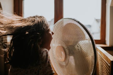 a little girl enjoys cool air blowing in her face from an old fashioned large desk fan