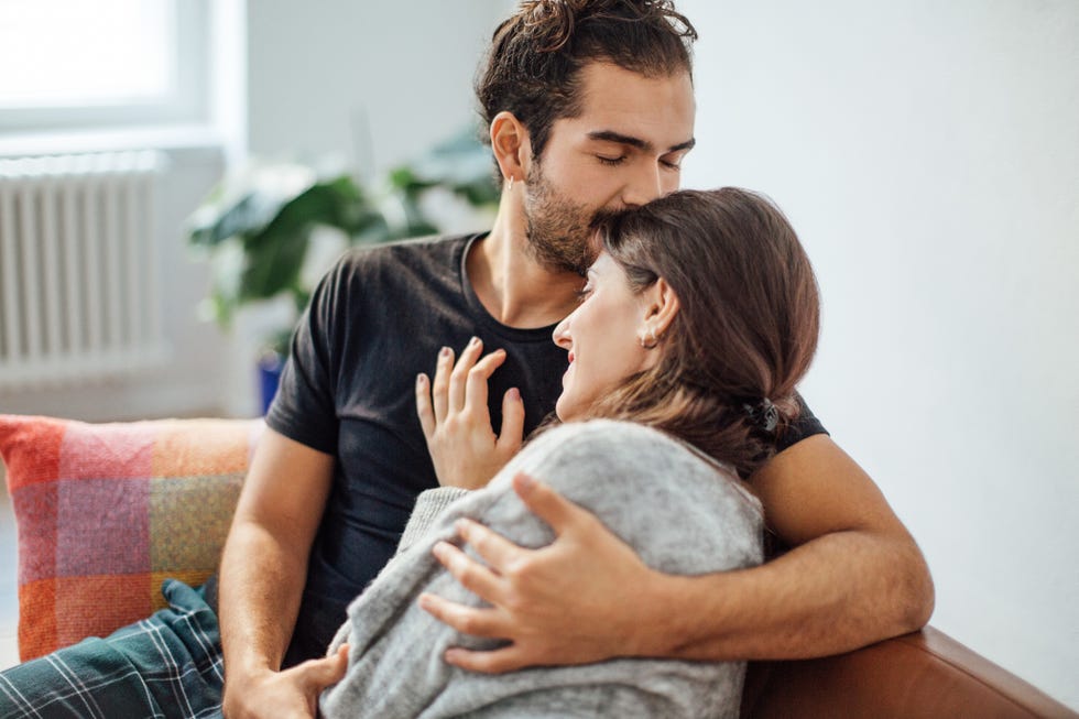 man embracing girlfriend while kissing on her forehead at home