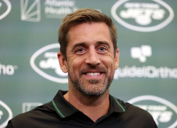aaron rodgers smiles at the camera, he wears a black polo shirt with a green accent on the collar