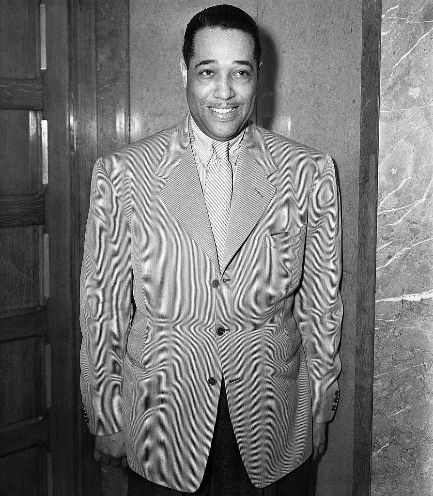 duke ellington smiling as he stands with his arms at his sides in a photo