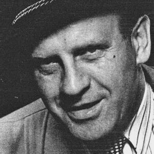 oscar schindler smiles and wears a hat, collared shirt, tie, and jacket