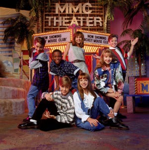 a group of kids stands and sits in front of a fake marque advertising the all new mickey mouse club