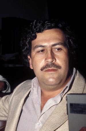 pablo escobar looks away from the camera, he is wearing a sport jacket and a collared shirt and has his signature large mustache