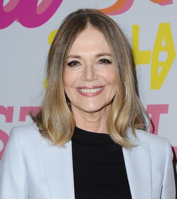 peggy lipton smiles at the camera, she wears a light colored suit jacket and black shirt