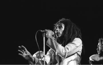 bob marley holding a microphone with his left hand and looking out toward an audience as he sings