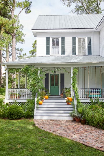 white house exterior with dark shutters and wrap around porch and brick pathway