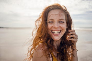 portrait of a redheaded woman, laughing happily on the beach