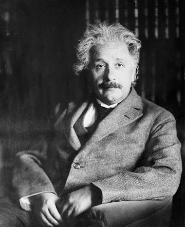 albert einstein sitting in front of a bookcase with his arms folded