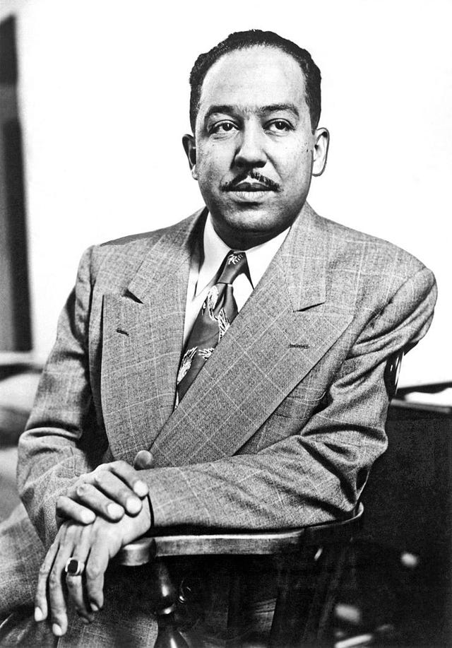 langston hughes sits and looks right of the camera, he wears a suit jacket, collared shirt, and patterned tie