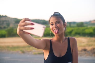 Portrait of teenage girl taking selfie with smartphone while sticking out tongue