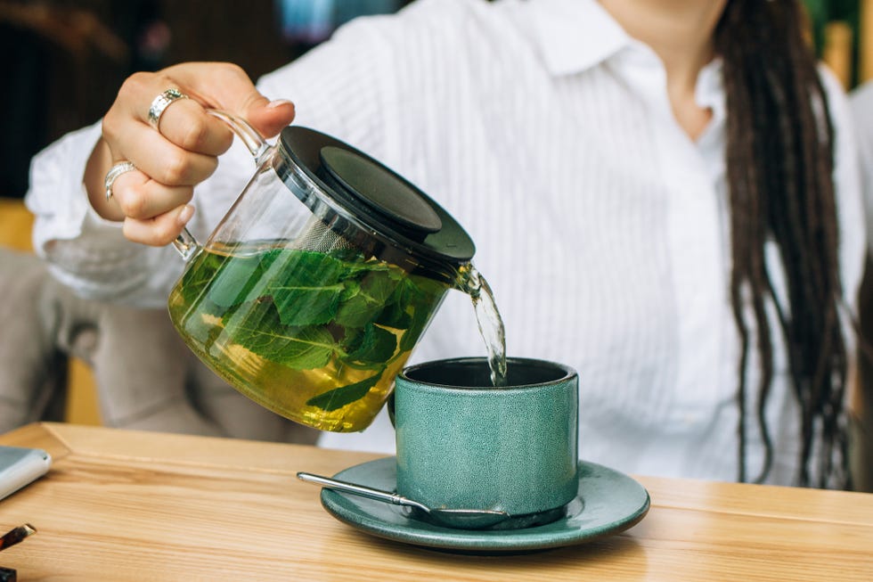 pouring green tea with mint from a glass teapot