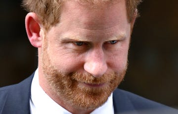 a close up of prince harry's face, looking off camera and appearing thoughtful, while wearing a blue suit