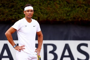 rafael nadal stands with his hands on his hips, he wears all white, including a white headband, and a watch