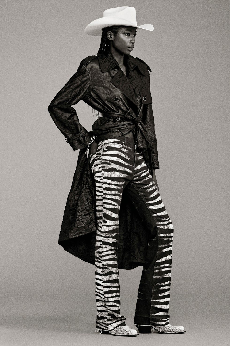 Fashion model wearing a black leather trench coat and zebrastriped pants with a cowboy hat